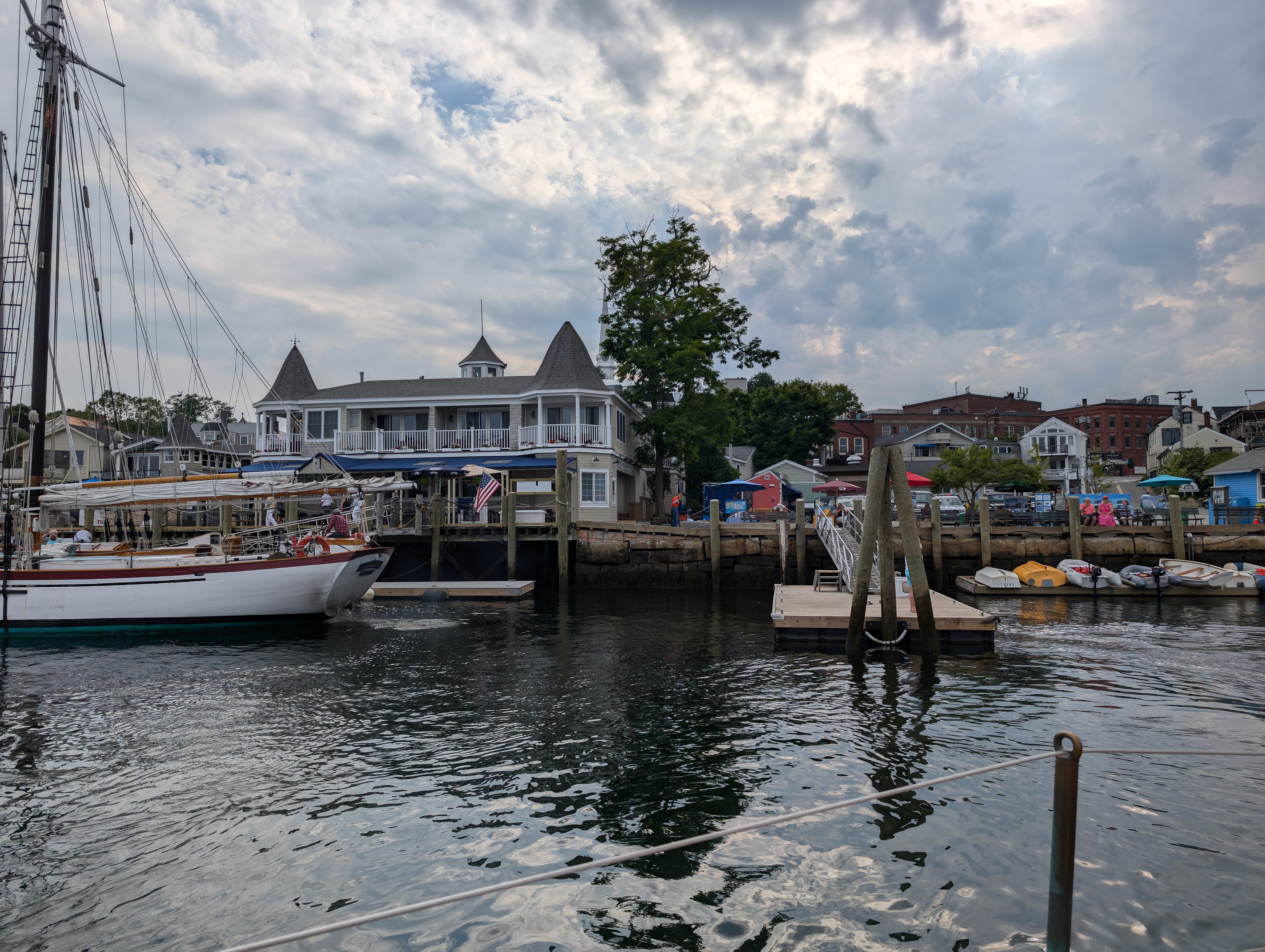 looking into a pier from the about 20 feet from the dock. Various stands on the right. Building in the center houses a restaurant with wrap around balconies and seating. Old fashioned sailboat on the left edge of the photo