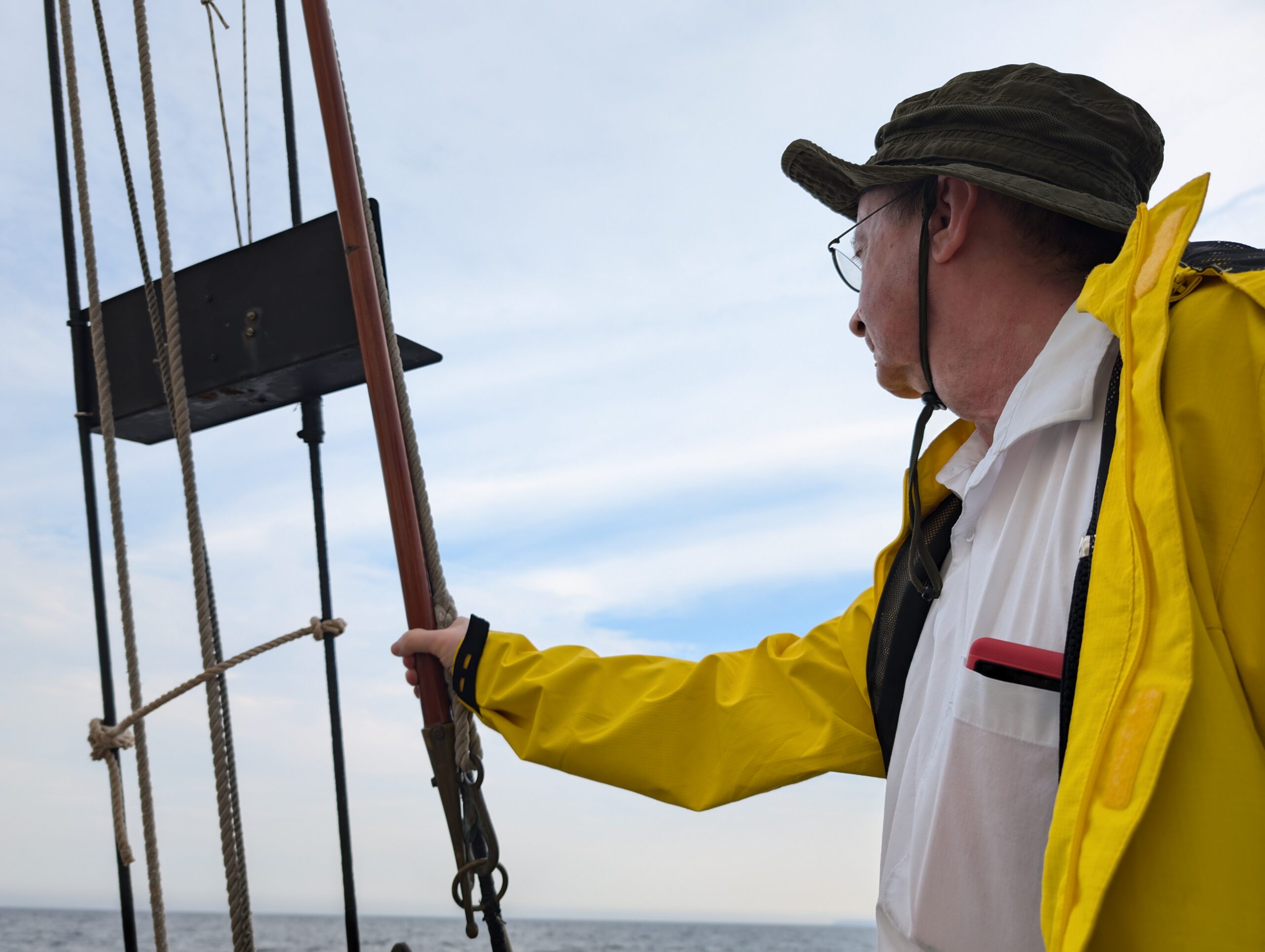 My dad in a yellow jacket holding onto some rope while looking out onto an overcast sky