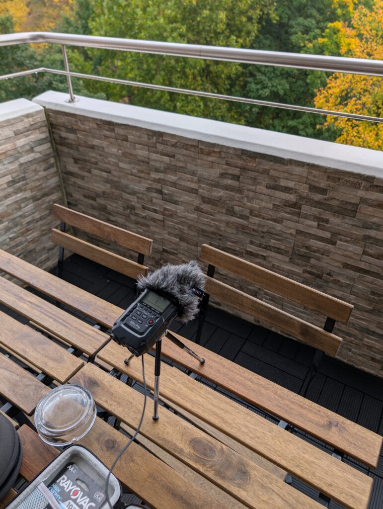 Picture of my zoom H4n microphone recording the wooded area outside of the airbnb. The microphone is sitting on wooden table that is on the balcony.