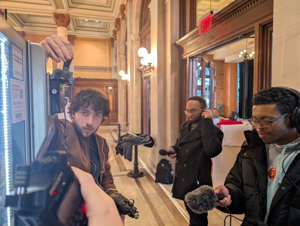 A group of 3 individuals, pointing their microphones at a vending machine